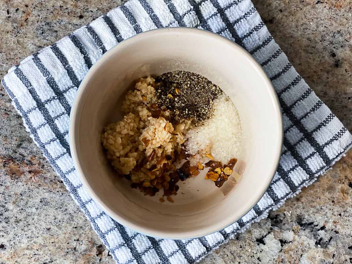 Top down shot of spices and seasonings and garlic in a small seasoning bowl.