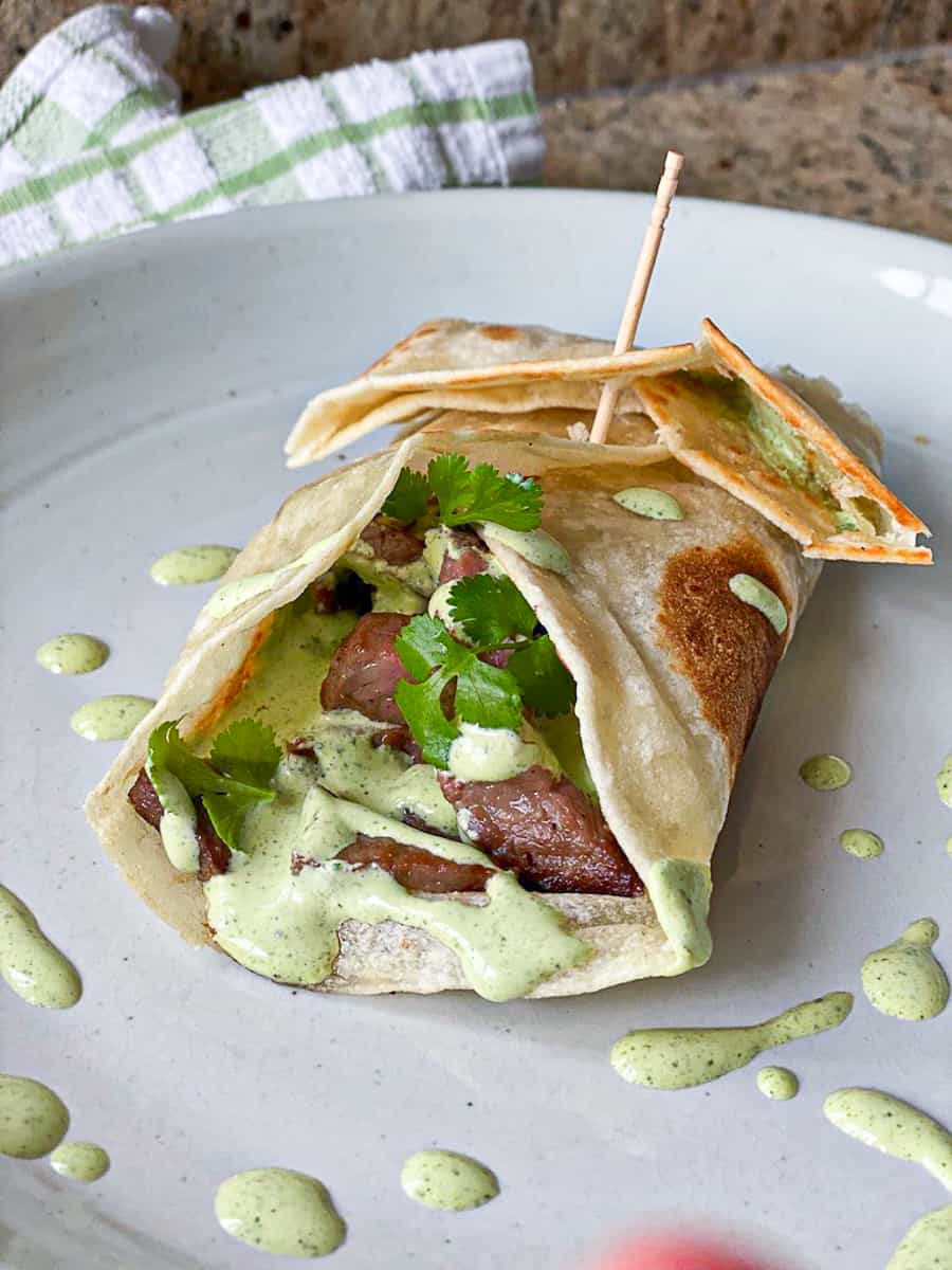 Side shot of steak taco sous vide style with cilantro dressing seasoning on a plate.