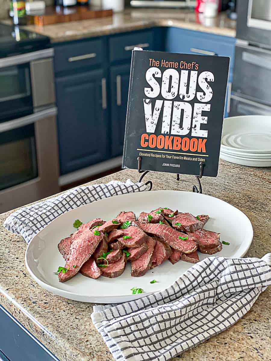 Side shot of the home chef's sous vide cookbook with sous vide steak seasoned with fresh herbs.