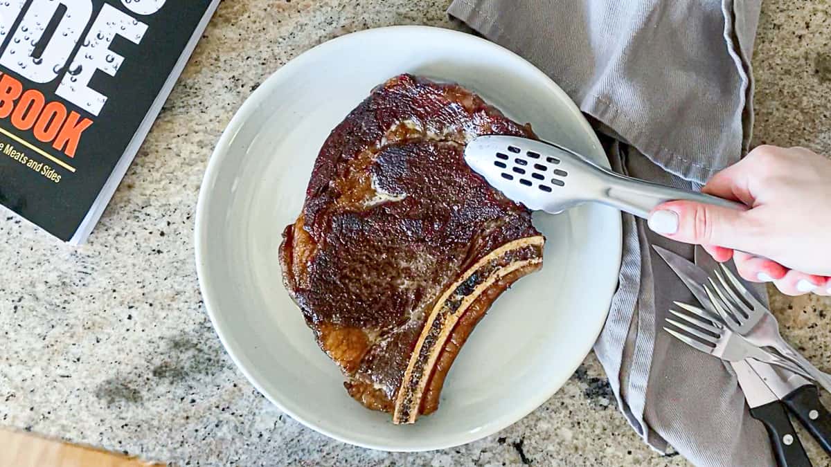 Top down shot of tongs adding mayo sear seasoned sous vide steak to a plate.