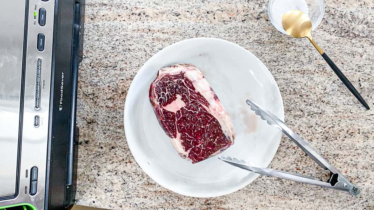 Top down shot of vacuum sealer with raw steak on a plate with salt seasoning.