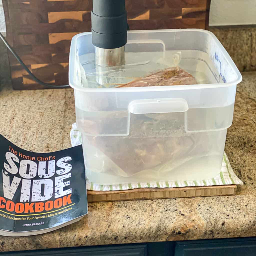 Side shot of sous vide cooking pork loin in water with the home chef's sous vide cookbook.