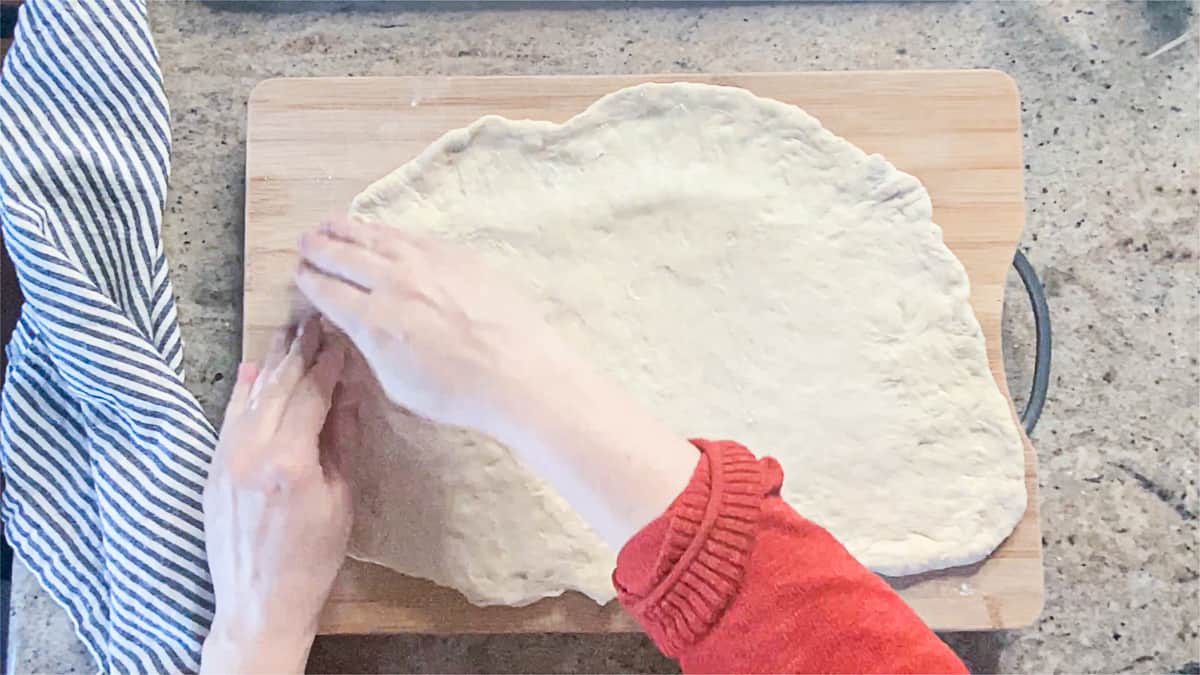 Top down shot of hands stretching ball of pizza dough on a counter.
