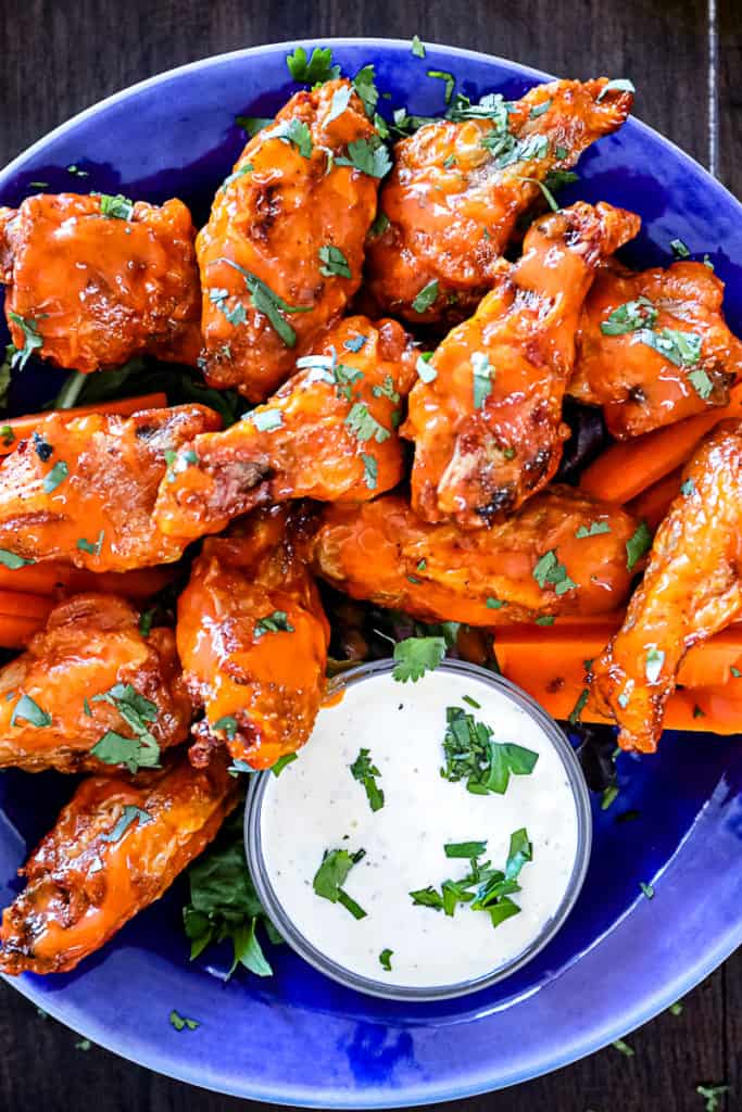 Top down shot of hot buffalo air fryer chicken wings with blue cheese dip and cilantro on a plate.