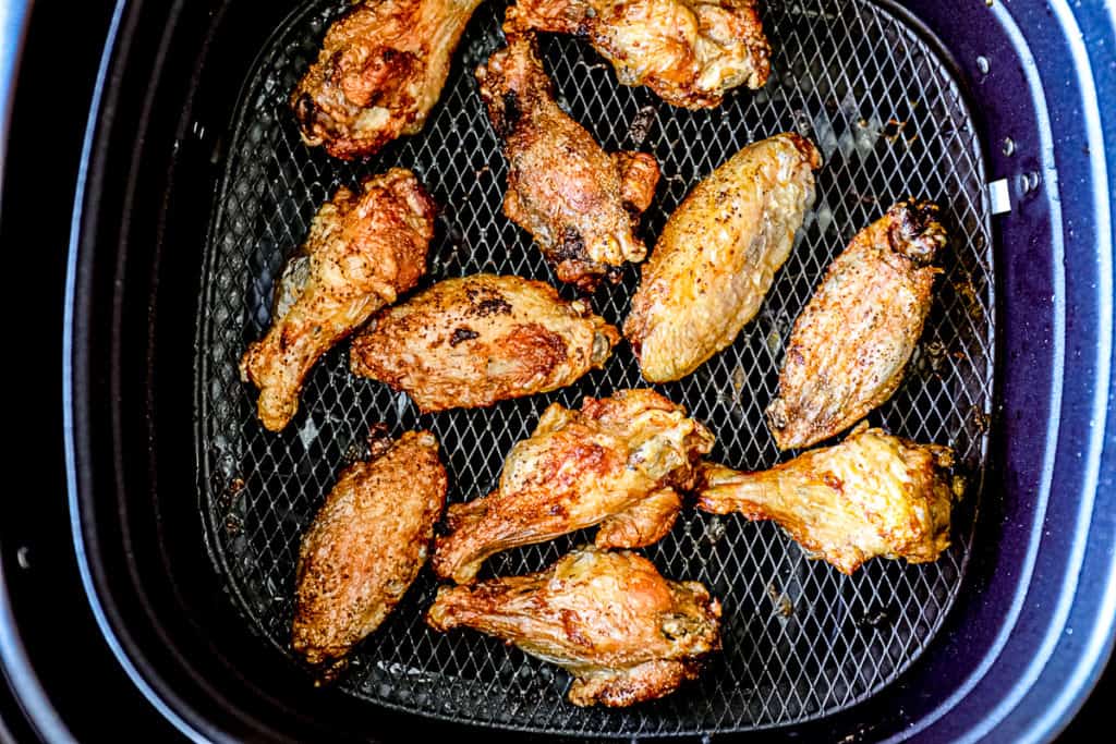 Top down shot of chicken wings cooking in air fryer basket with dry rub seasoning.