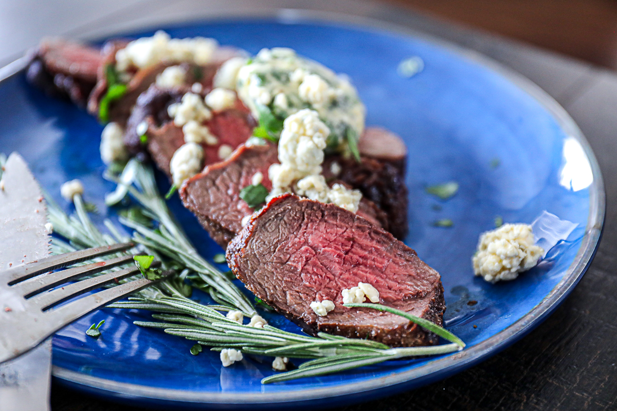 Shot of filet mignon air fried and cut on a plate with blue cheese crumbles and rosemary sprig.