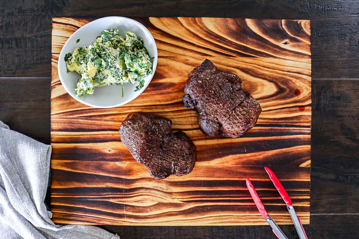 Filet mignon air fried and resting on a cutting board with a side of compound butter.