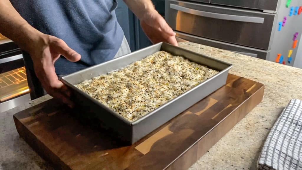 Side shot of hands holding focaccia bread dough in pan.