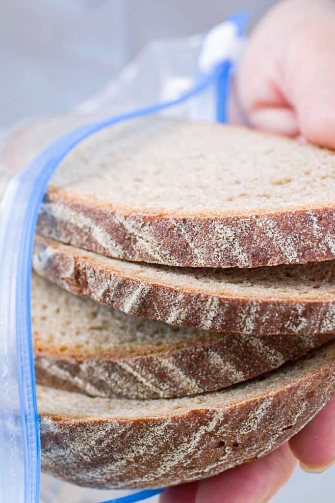 Side shot of hands freezing a loaf of bread in a ziplock plastic bag.