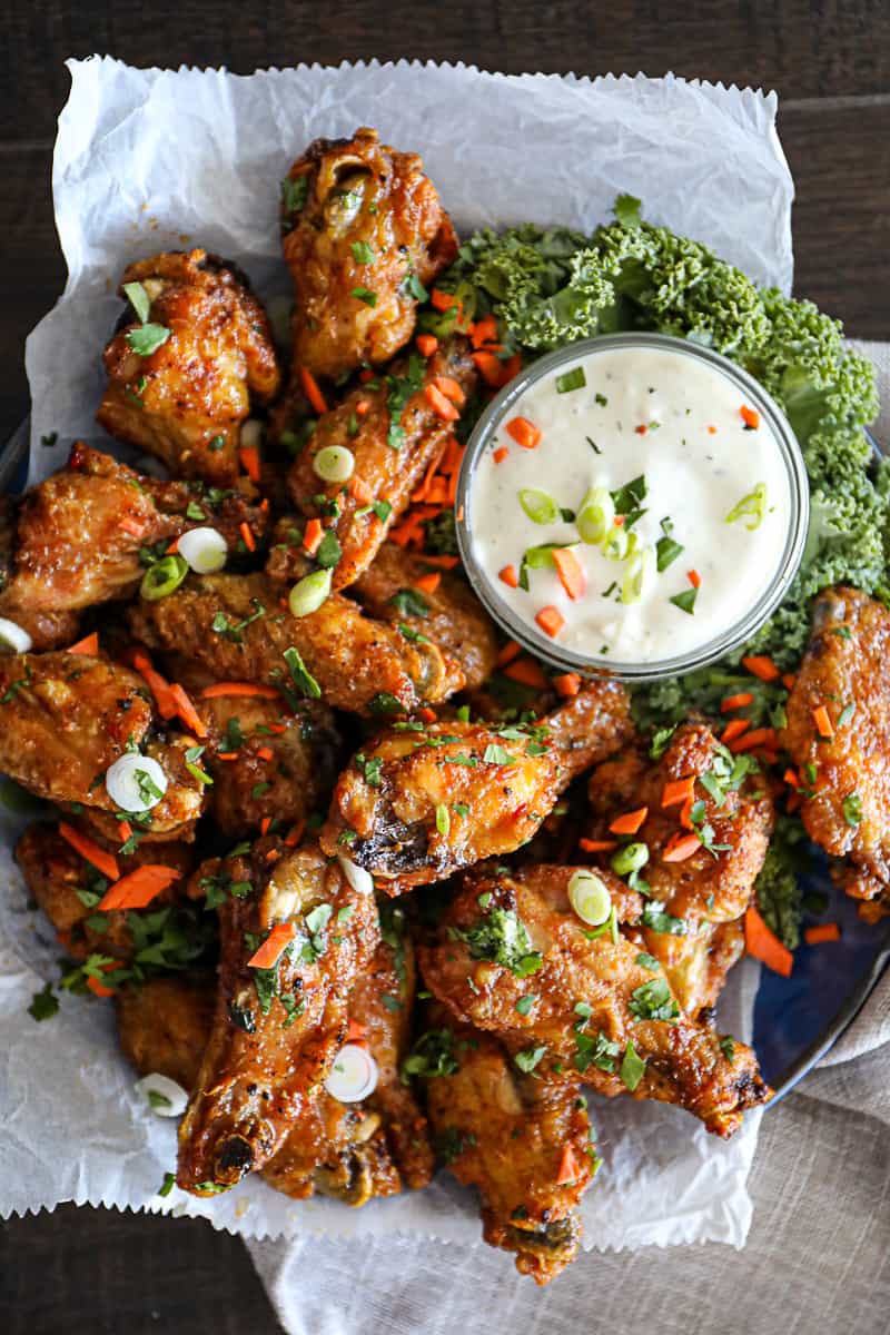 Top down shot of crispy oven baked chicken wings with carrots and cilantro on a plate with blue cheese dip.