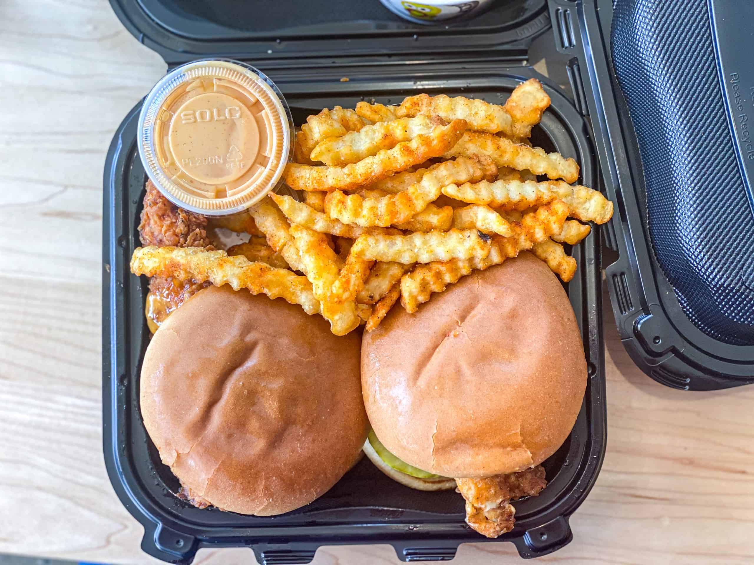 Top shot of dave's sauce with crinkle cut french fries and Nashville style hot chicken sandwiches.