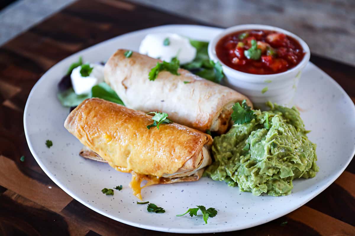 Side shot of cheese melted on air fryer frozen burrito with a side of salsa and guacamole.