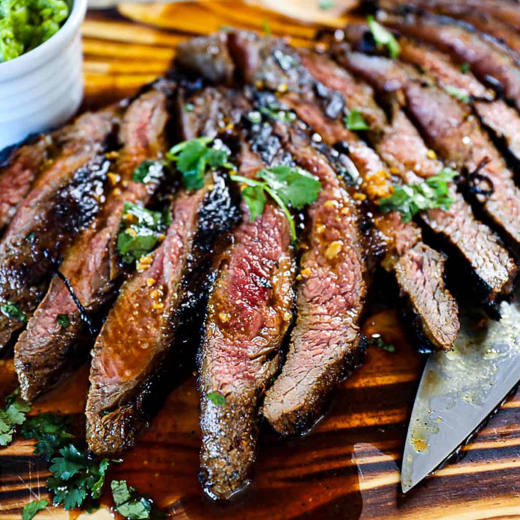 Side shot of Flank Steak Marinade on medium rare steak with cilantro and fresh ginger on a cutting board.