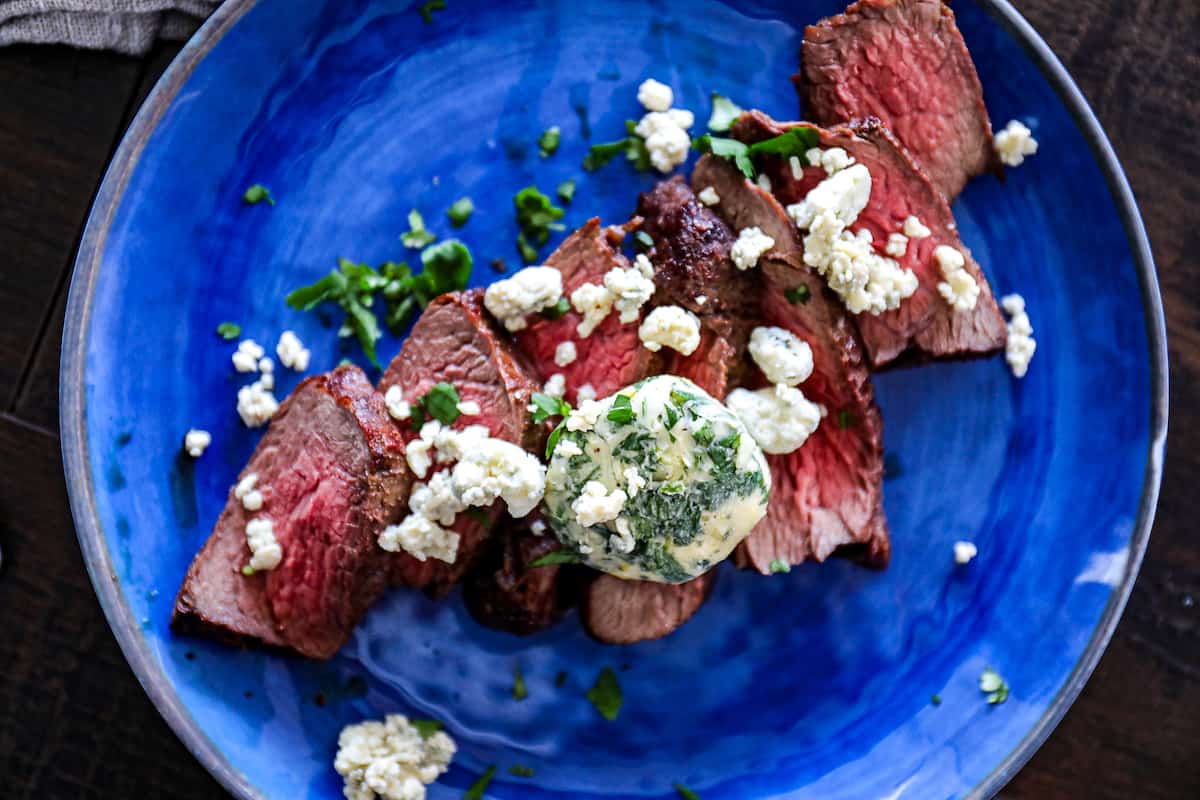 Top down shot of a slab of compound butter log on sliced steaks on a plate with blue cheese.