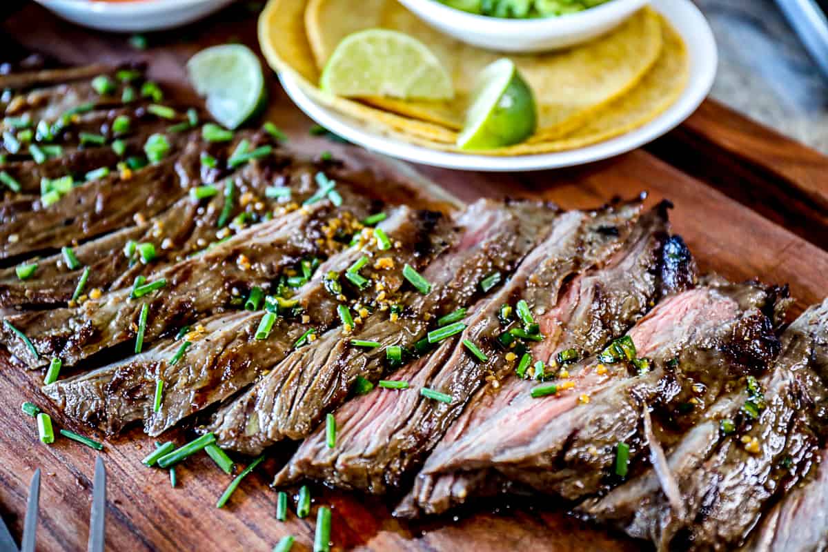 Side shot of platter of skirt steak for tacos with corn taco shells and limes.