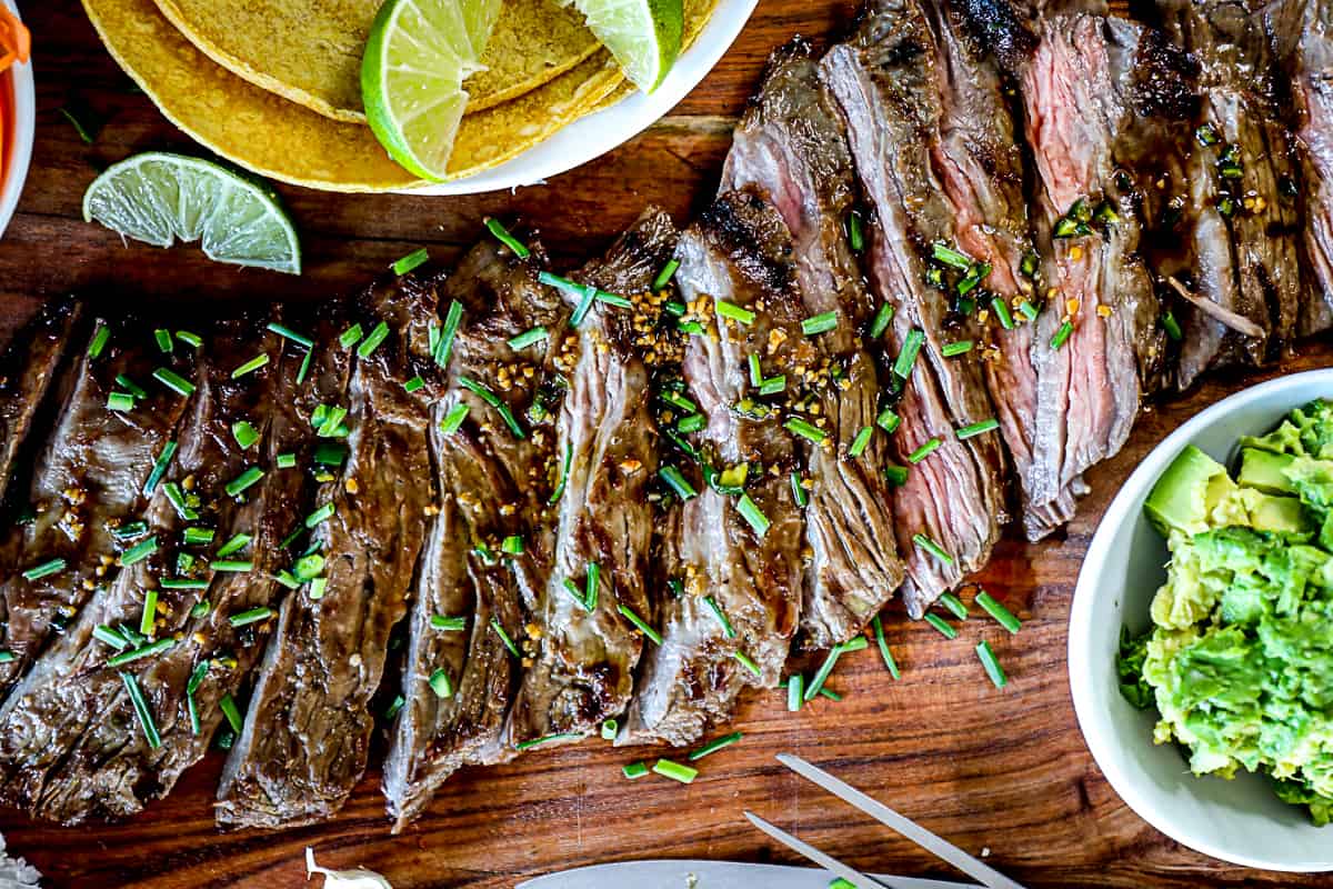 Top down shot of sliced grilled skirt steak with taco ingredients on a serving board.