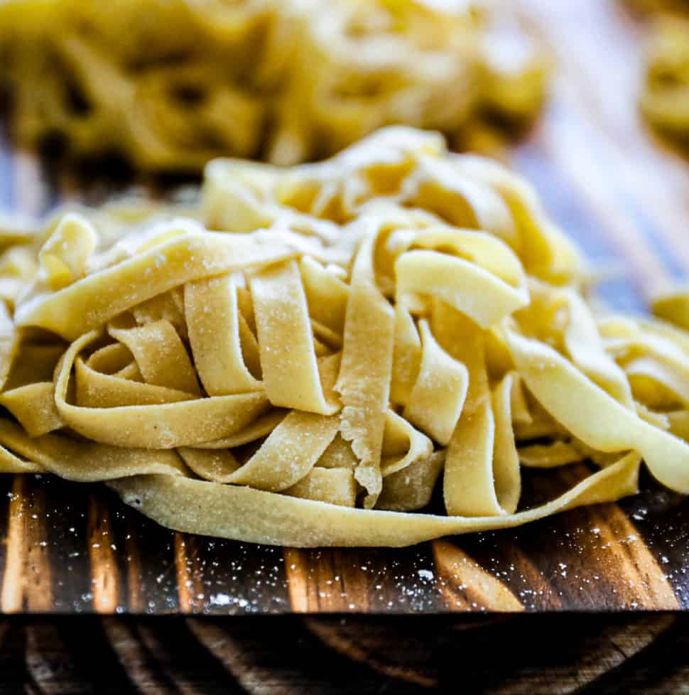 Side shot of homemade Pasta Recipe Fettuccine, Linguine, Spaghetti Sip Bite Go fresh pasta noodles on a cutting board.