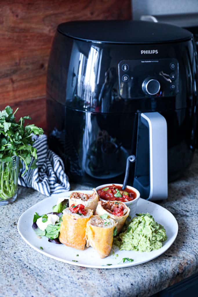 Side shot of cooked frozen food next to air fryer machine phillips xl.