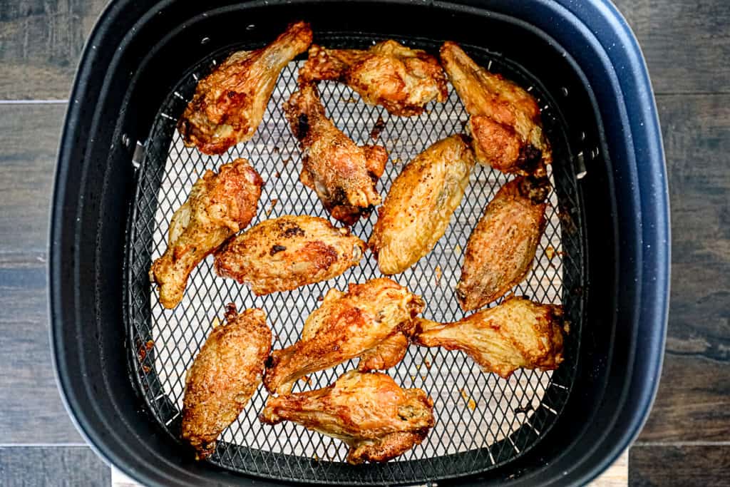 Top down shot demonstrating cooked food in an air fryer basket with chicken wings.