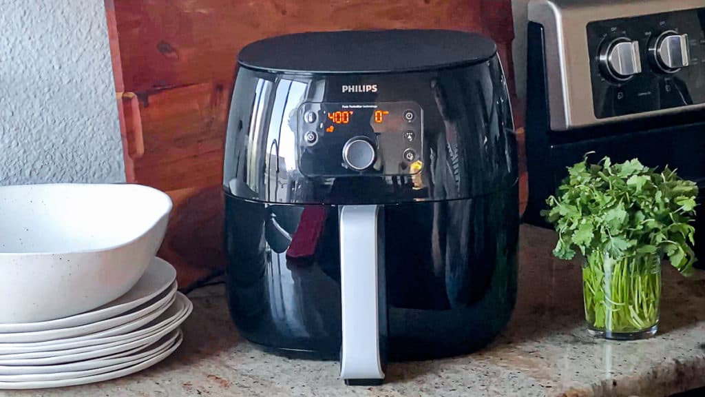 Side shot of phillips air fryer xl machine on a counter with plates and fresh herbs.