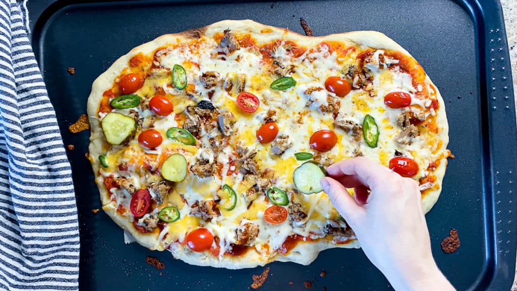 Top down shot of hand adding pickles to pulled pork pizza