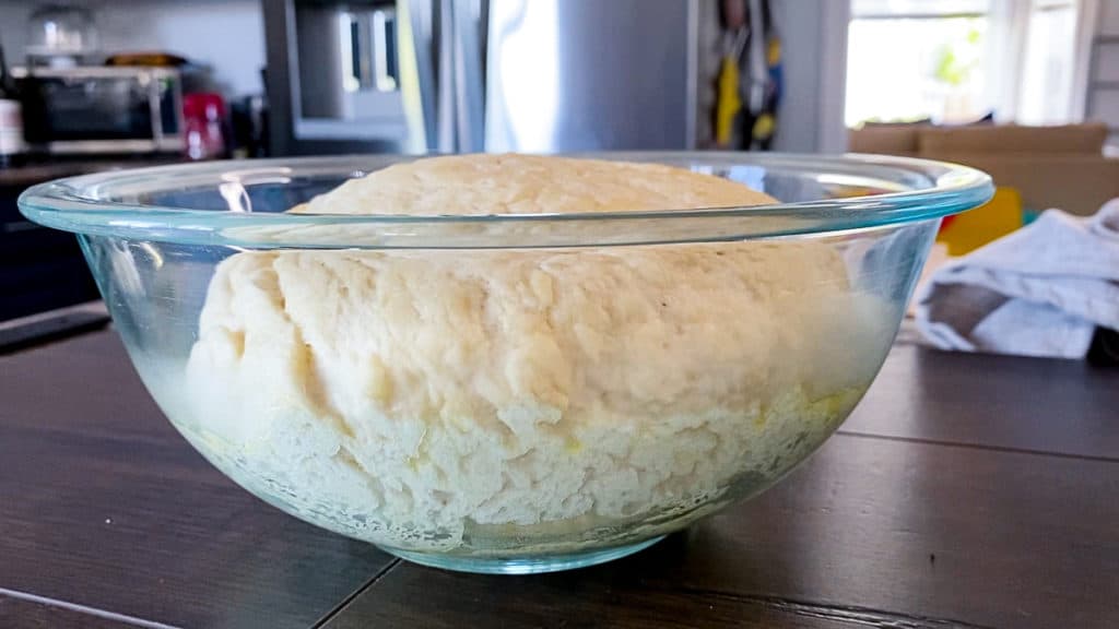 Side shot of light and fluffy homemade pizza dough in a glass bowl.