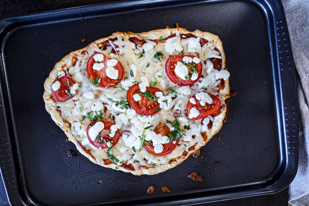 Top down shot of freshly baked homemade pizza dough crust with tomatoes and mozzarella toppings.
