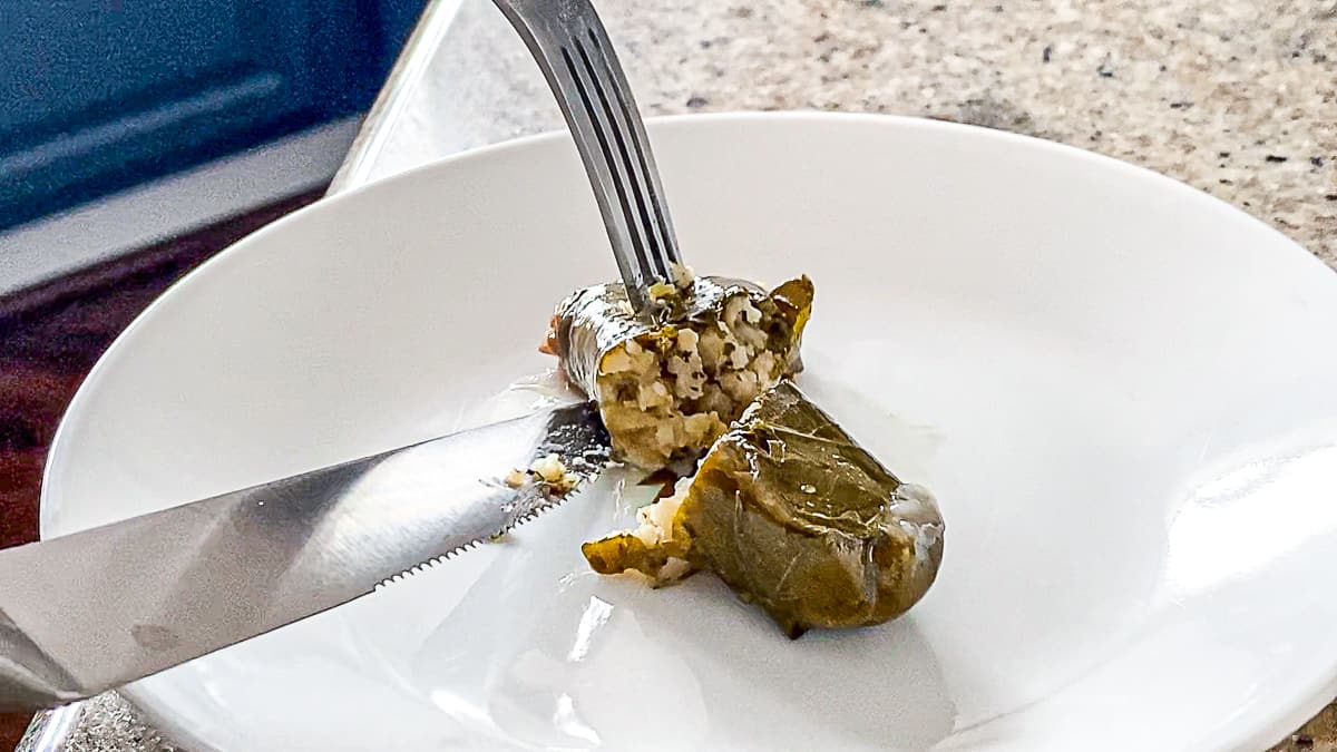 Side shot of fork and knife cutting open a stuffed grape leaf with rice from Trader Joe's.