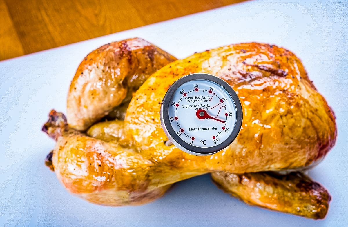 Demonstrating roasted Whole Chicken temperature checking with an internal thermometer stuck in it.