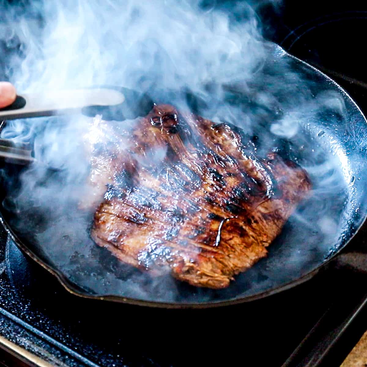 Side shot of Flank Steak searing in a cast iron skillet.