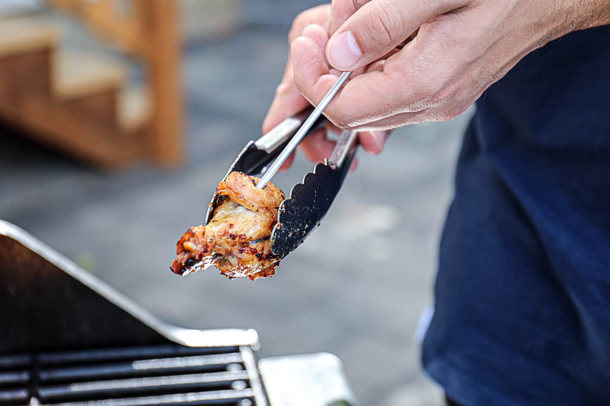 Instant read thermometer taking temperature of cooked chicken wings grilled.