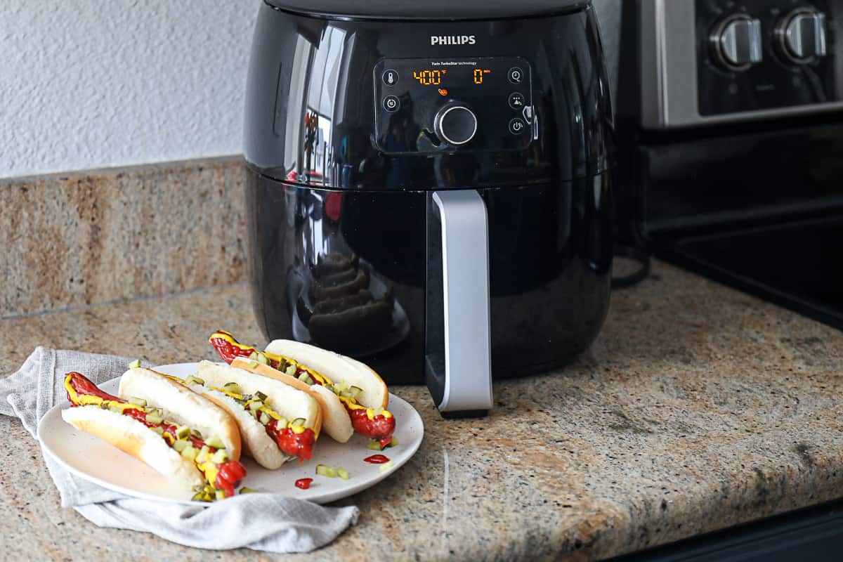 Phillips air fry machine next to air fried hot dogs on a plate.