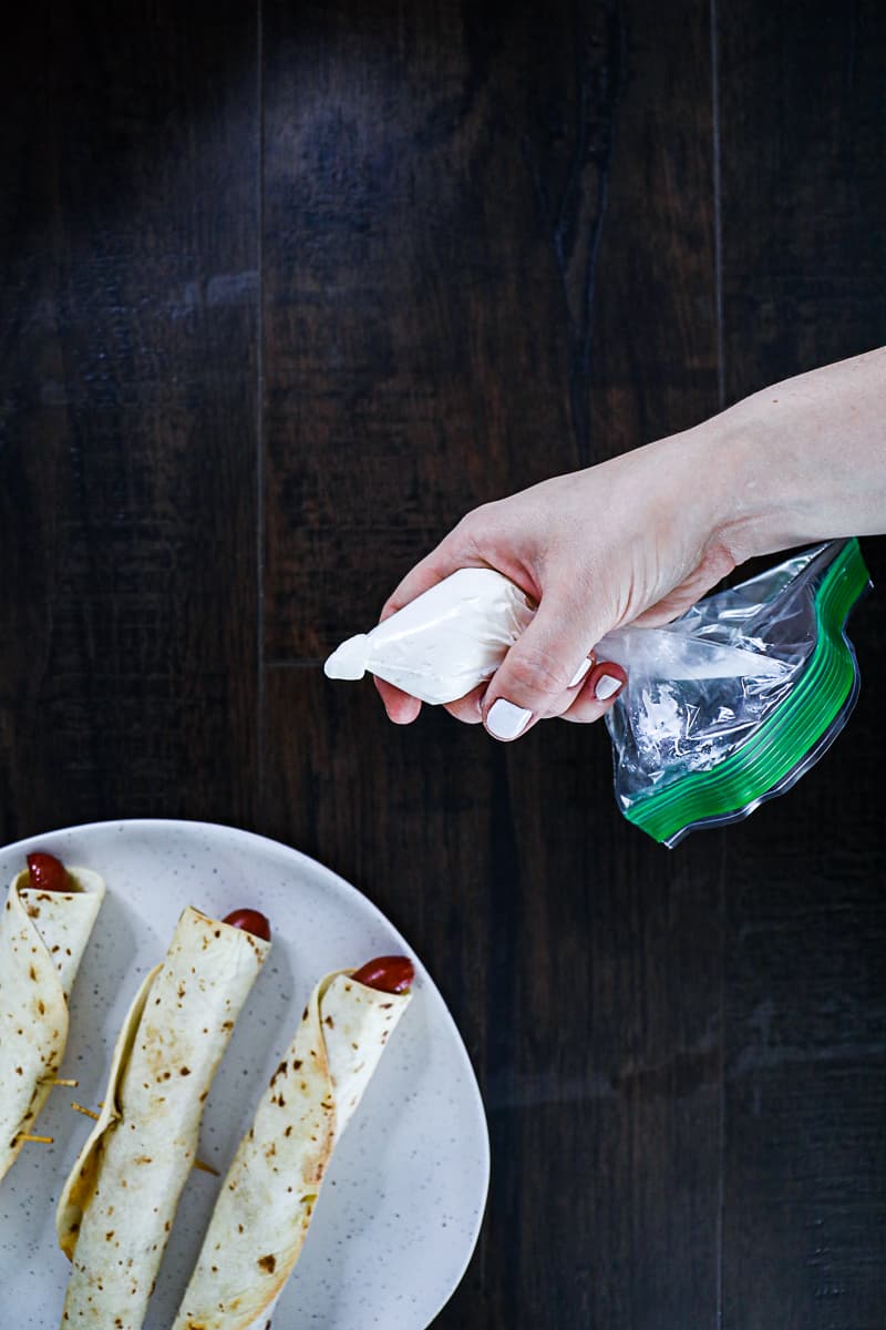 Squeezing sour cream in ziplock bag to put on hot dog tortillas.