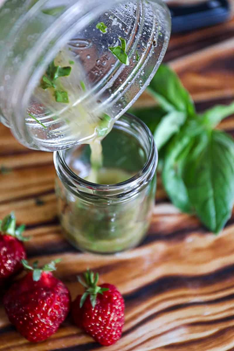 Side shot of pouring salad dressing from a bell jar to a serving jar.