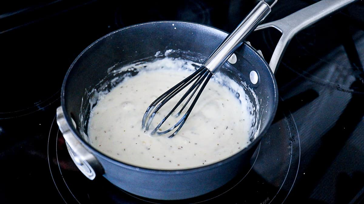 Top down shot of cooking creamy white cheese sauce in pan with a whisk.