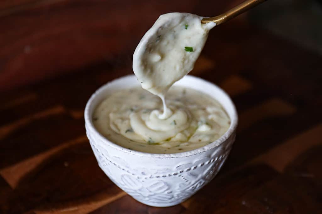 Side shot of garlic white sauce in a sauce bowl with a spoon.