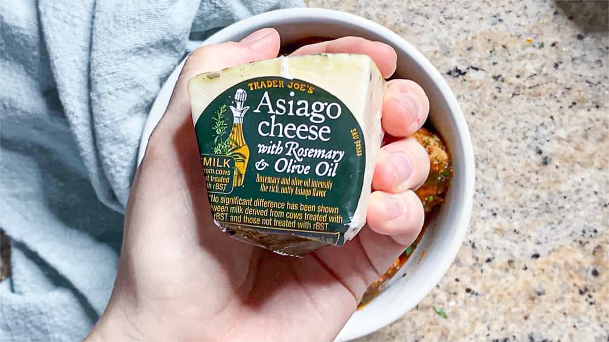 Top down shot of a block of trader joe's asiago cheese with rosemary and olive oil.