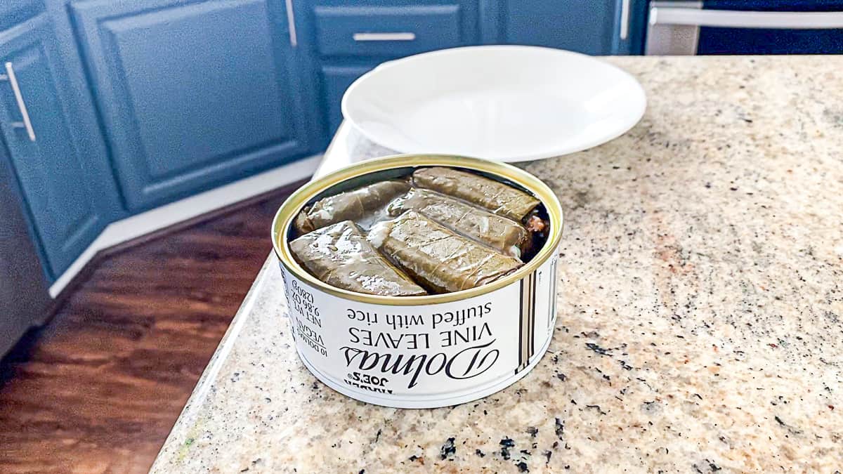 Side shot of open canned dolmas Trader Joe's white rice stuffed grape leaves on a counter with a plate..