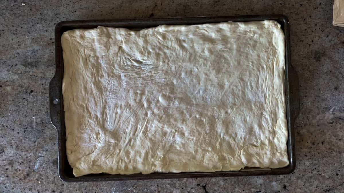 Top down shot of stretched raw pizza dough to a sheet tray.
