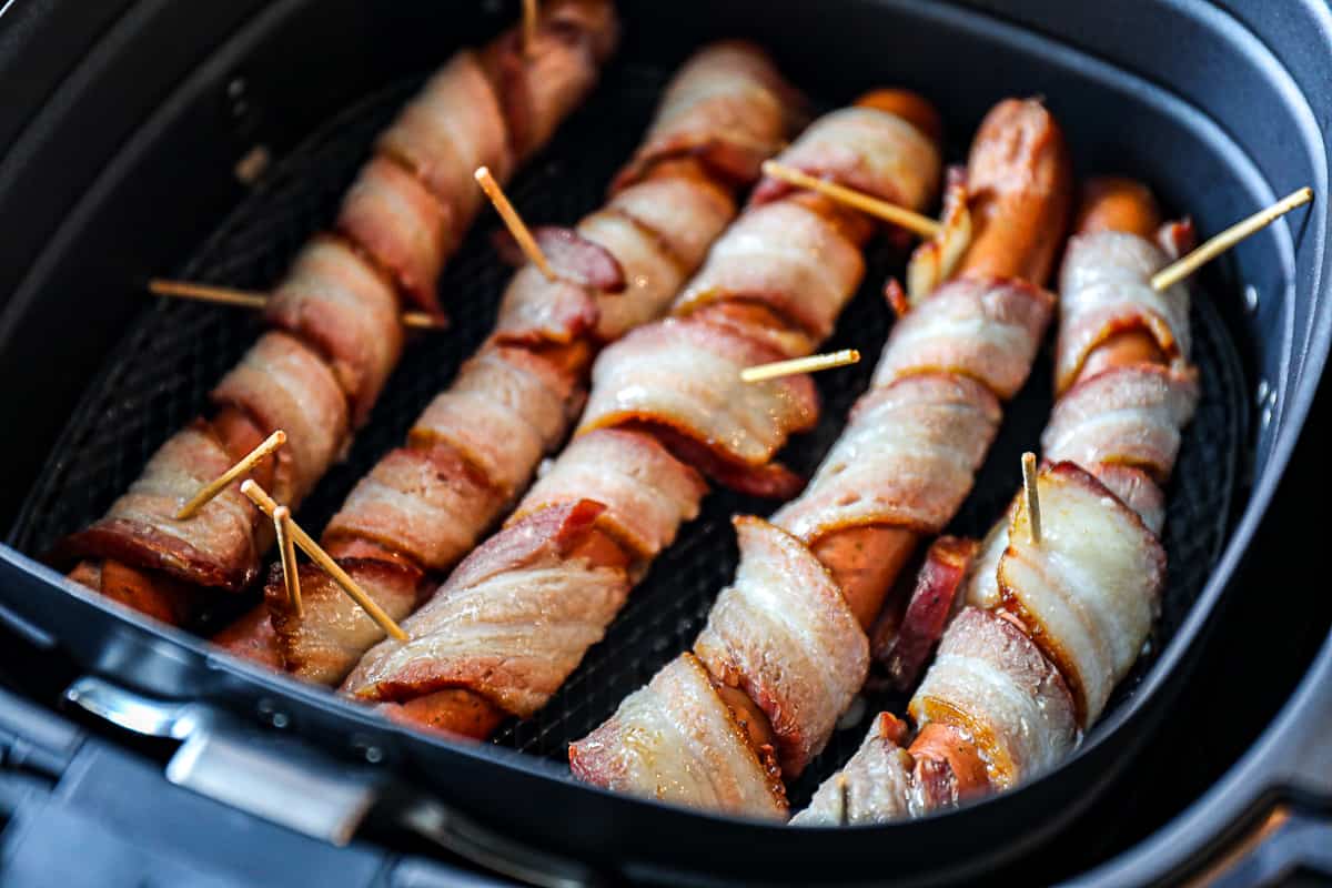 Raw Bacon Wrapped Hot Dogs In Air Fryer Basket.