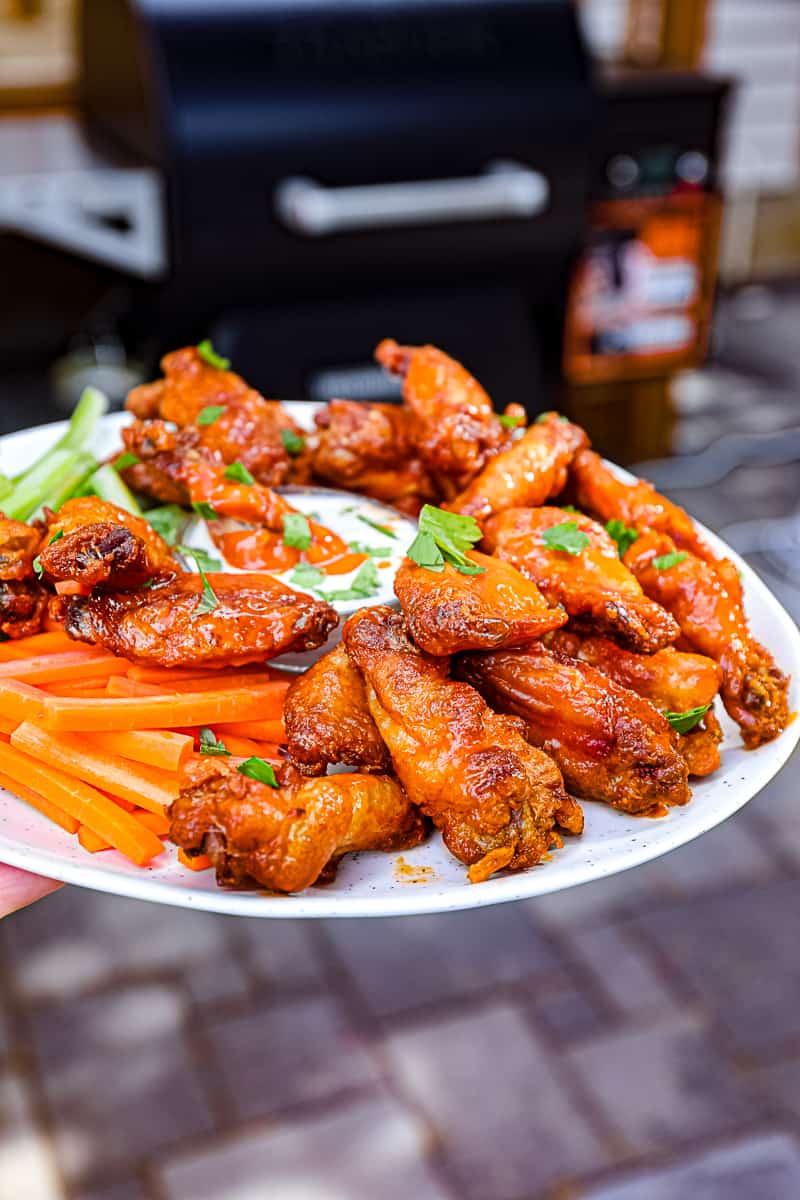 Closeup of smoked wings with Traeger smoking food in the background Sip Bite Go