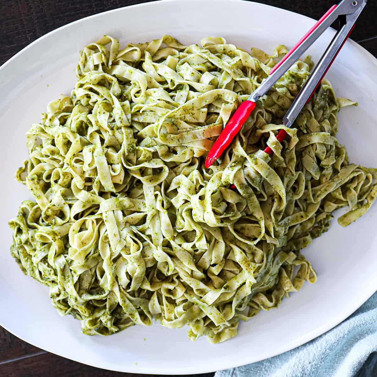 Fettuccine Pesto Pasta Recipe on a family style dinner serving platter with tongs.