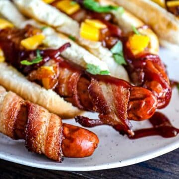 Cooked Bacon Wrapped Hot Dogs with cheddar cheese and bbq sauce.