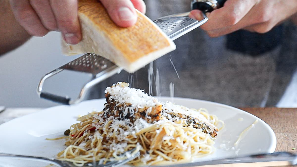 Parmesan cheese block grating over pasta and chicken dinner