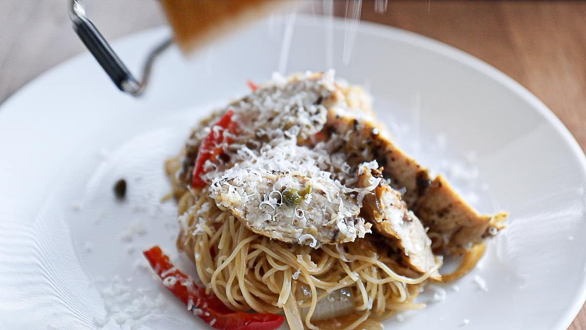 Parmesan cheese block grating over pasta and chicken dinner