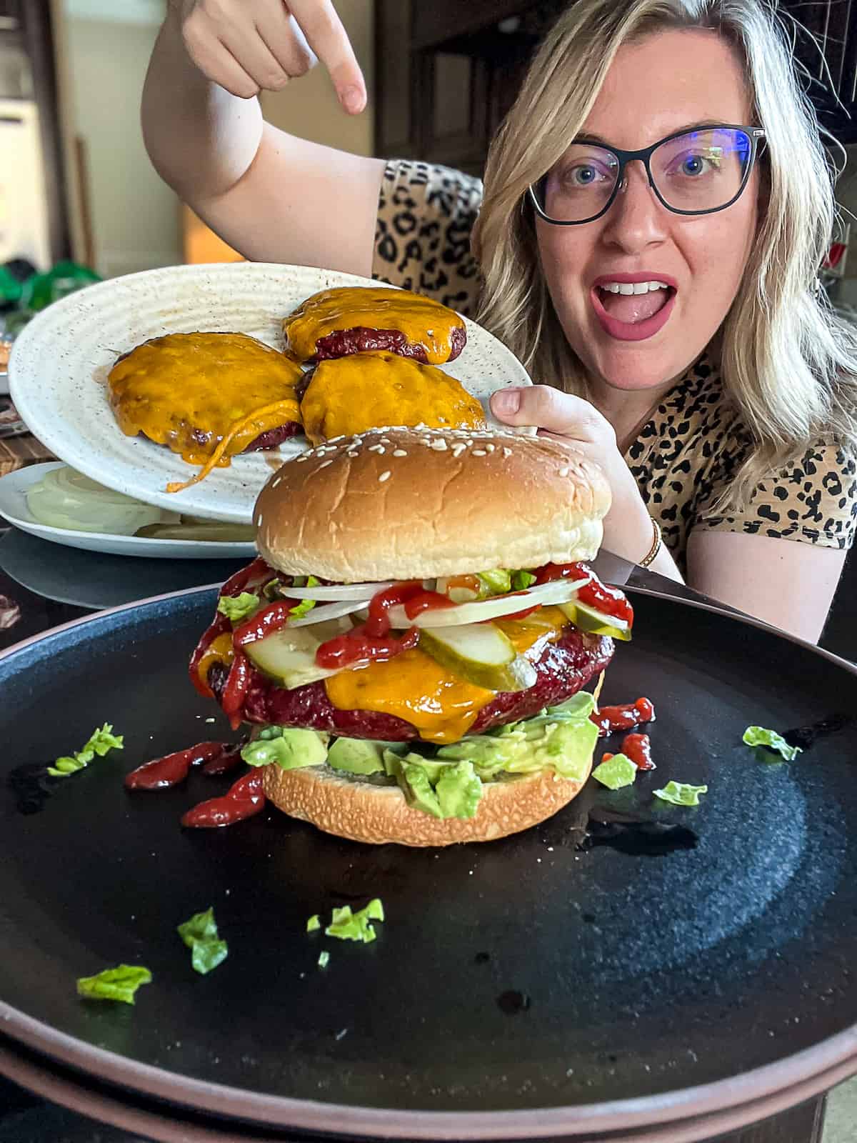 Jenna Passaro from Sip Bite Go holding smoked burger patties with cheese and a Traeger smoked burger with toasted buns