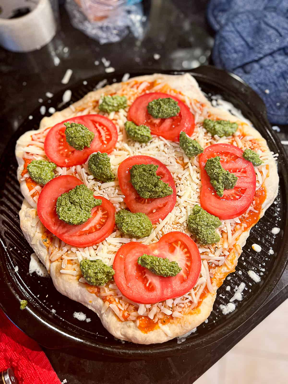 Raw ingredients including pesto and tomatoes on pizza dough