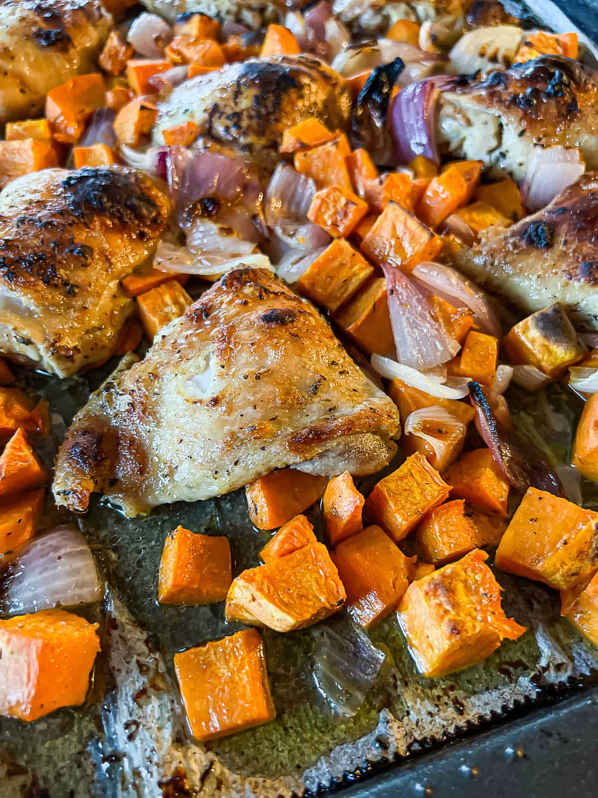 Closeup of broiled oven baked sheet pan chicken thighs with sweet potatoes