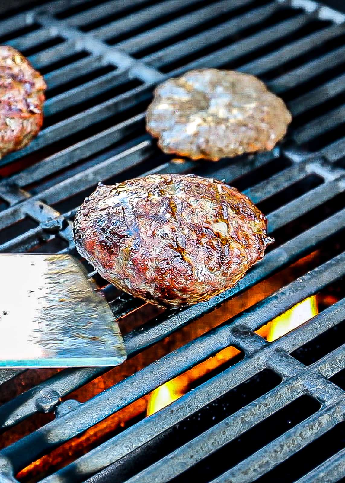 Demonstrating how to grill burgers on gas grill before flipping