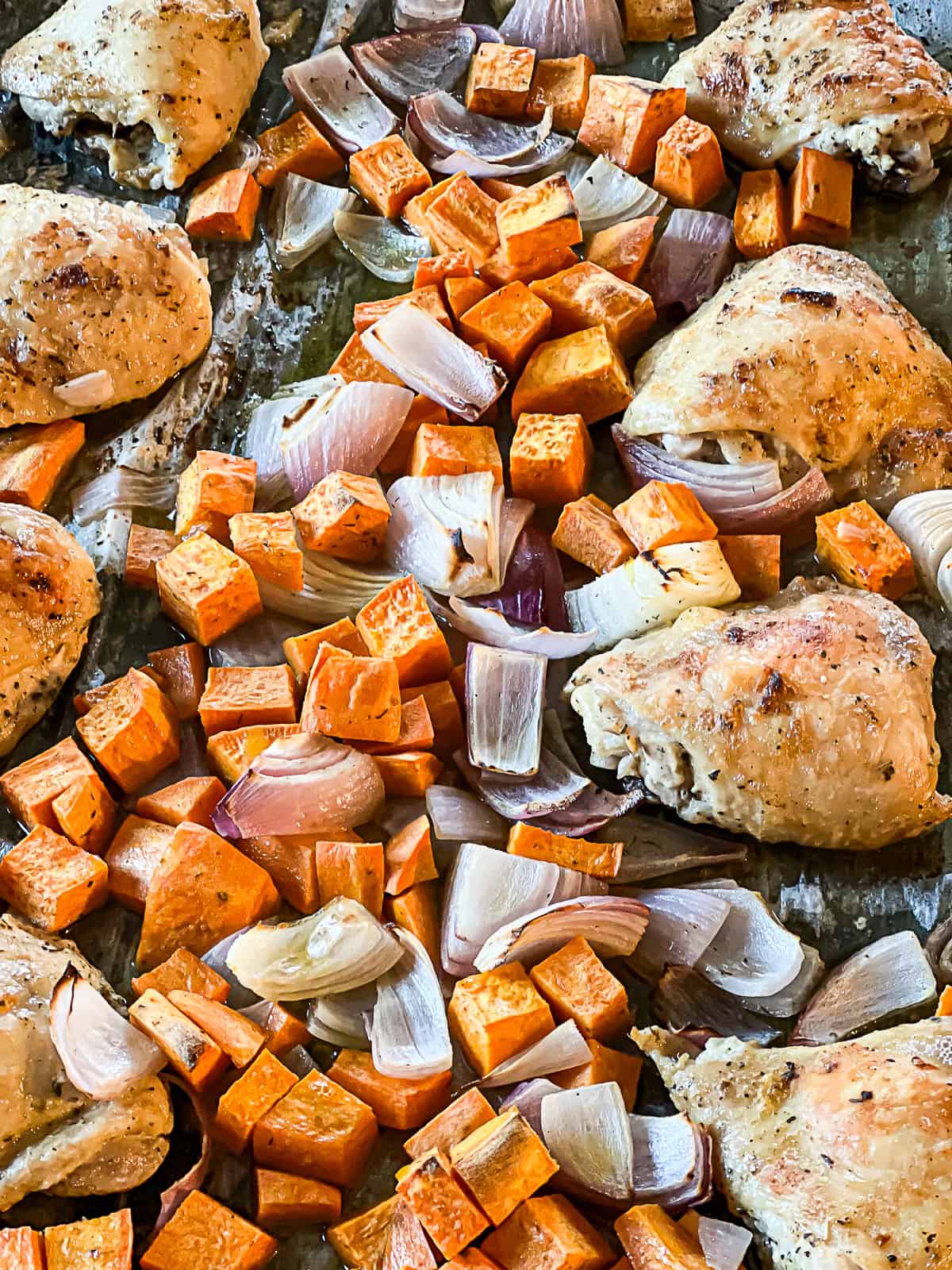 Oven Roasted Sheet Pan Chicken Thighs baking with sweet potatoes and red onions